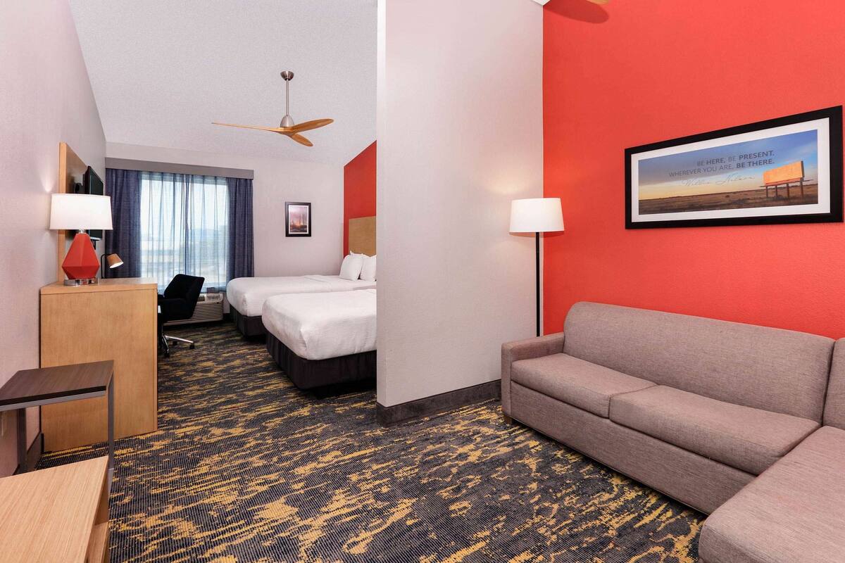 A hotel room with a bed, a sofa, a desk, and a desk lamp.