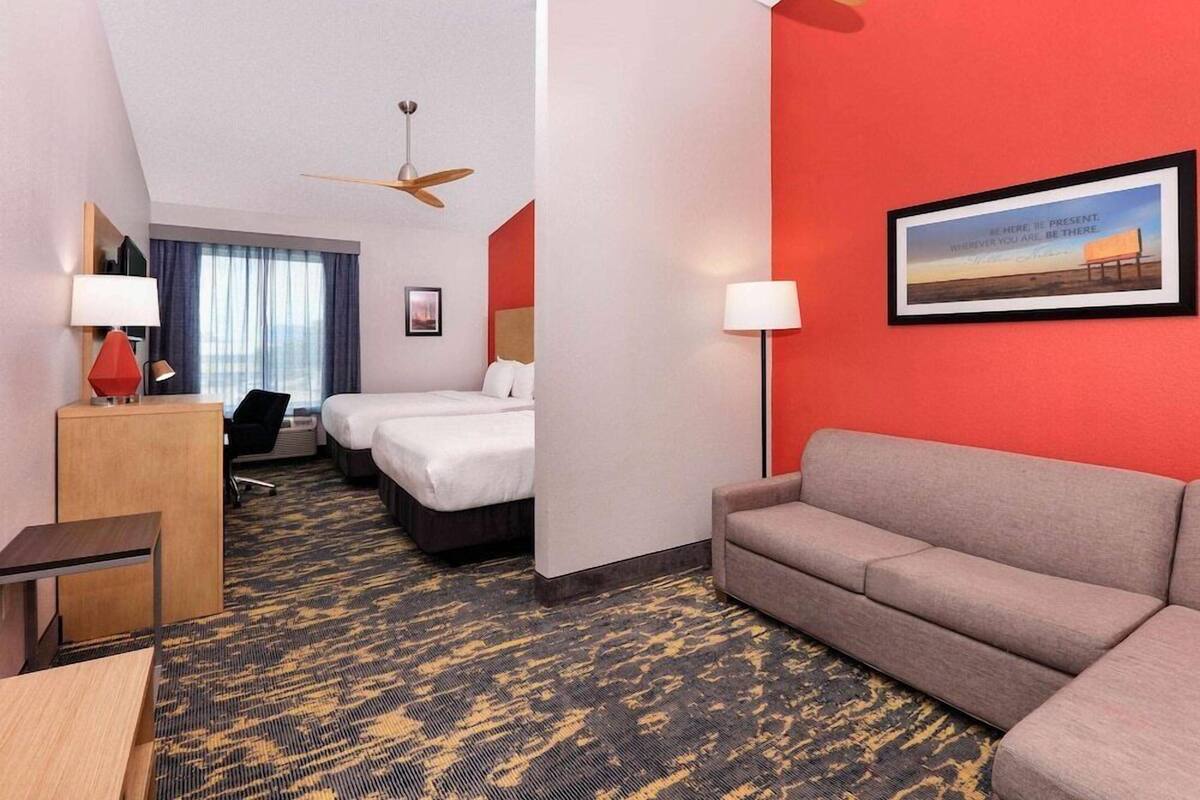 A hotel room with a bed, a sofa, a desk, and a ceiling fan.