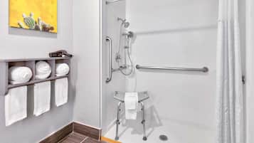 Zona de ducha con puerta de cristal, pasamanos, barra de apoyo y un taburete pequeño con una toalla.
