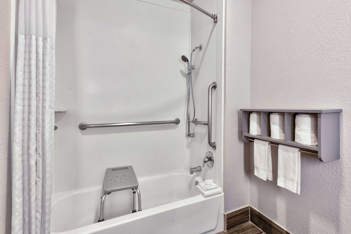 A bathroom with a bathtub, grab bars, a showerhead, and a towel rack.
