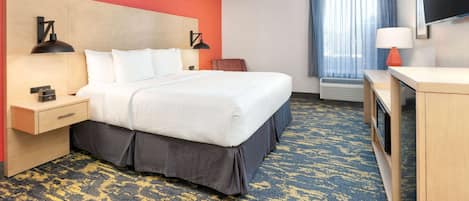 A hotel room with a large bed, a desk, a chair, a TV, and a window with curtains.