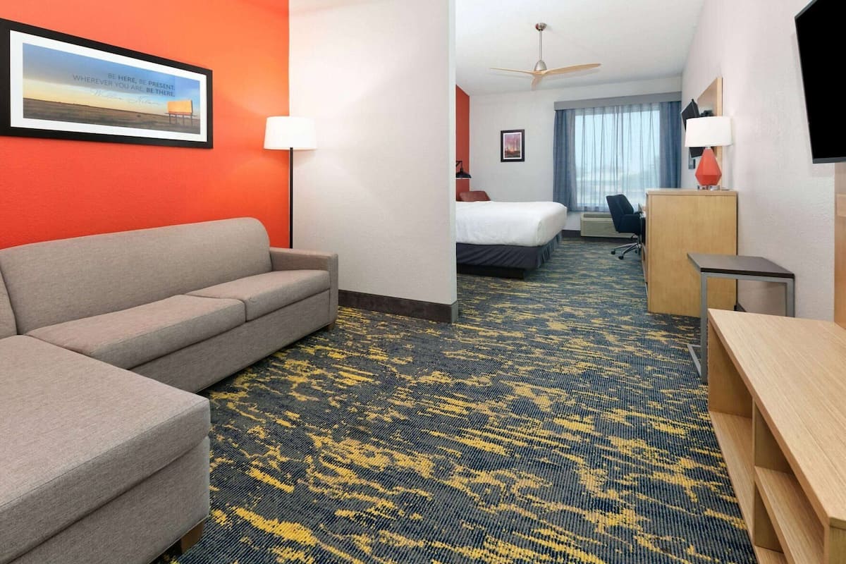 A hotel room with a sofa, a bed, a desk, a TV, and a ceiling fan.