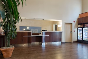 Un espace d’accueil avec un comptoir de réception en bois, une plante en pot, un réfrigérateur contenant des boissons et un panneau indiquant « Holiday Inn Express ».