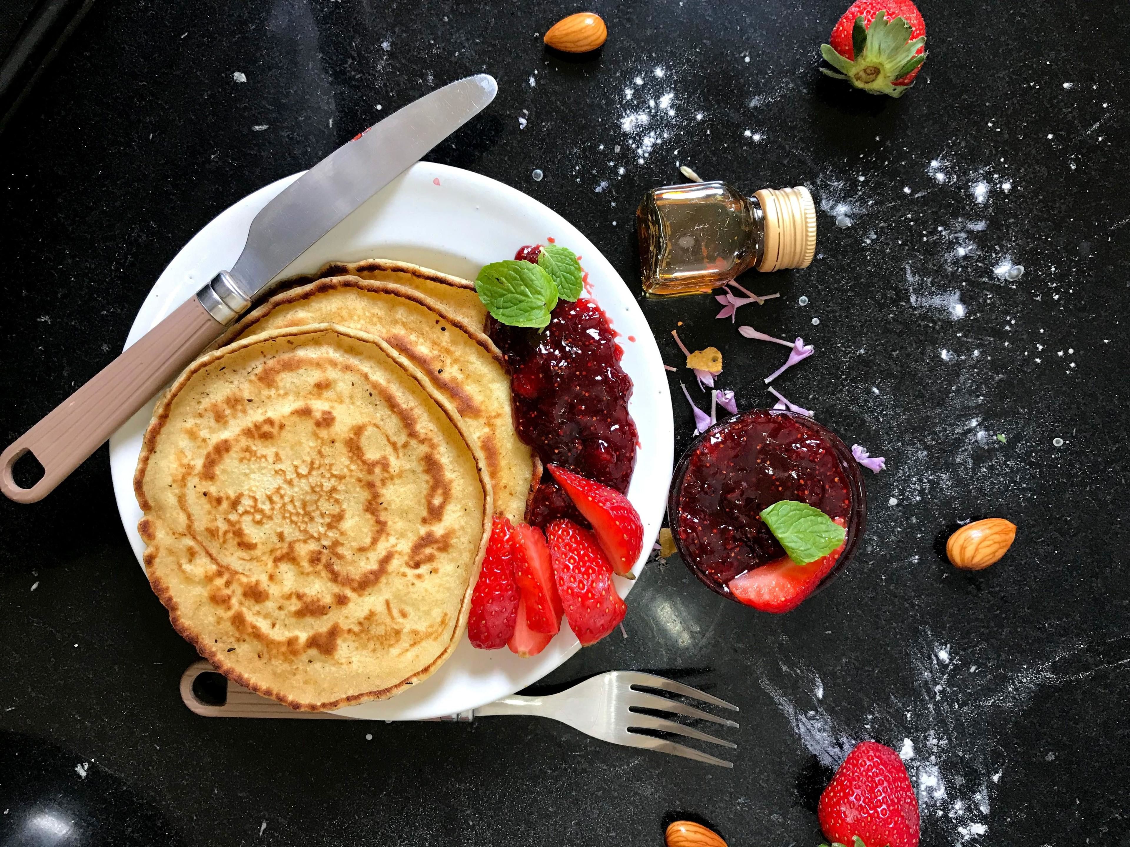 A plate of pancakes with strawberries and a small jar of jam.