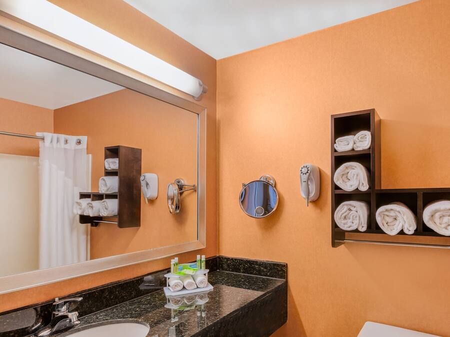 Un baño con un espejo grande, un lavabo, un perchero para toallas y una estantería con toallas.