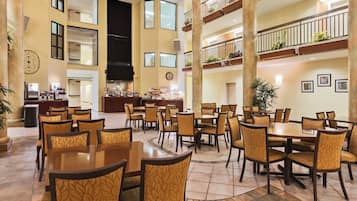 A spacious hotel lobby with multiple dining areas, a reception desk, and a large staircase connecting the floors.