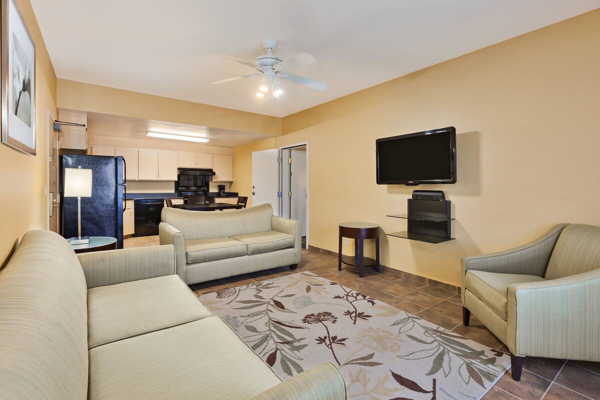 Una sala de estar con sofá, sillones, televisión de pantalla plana y ventilador de techo.