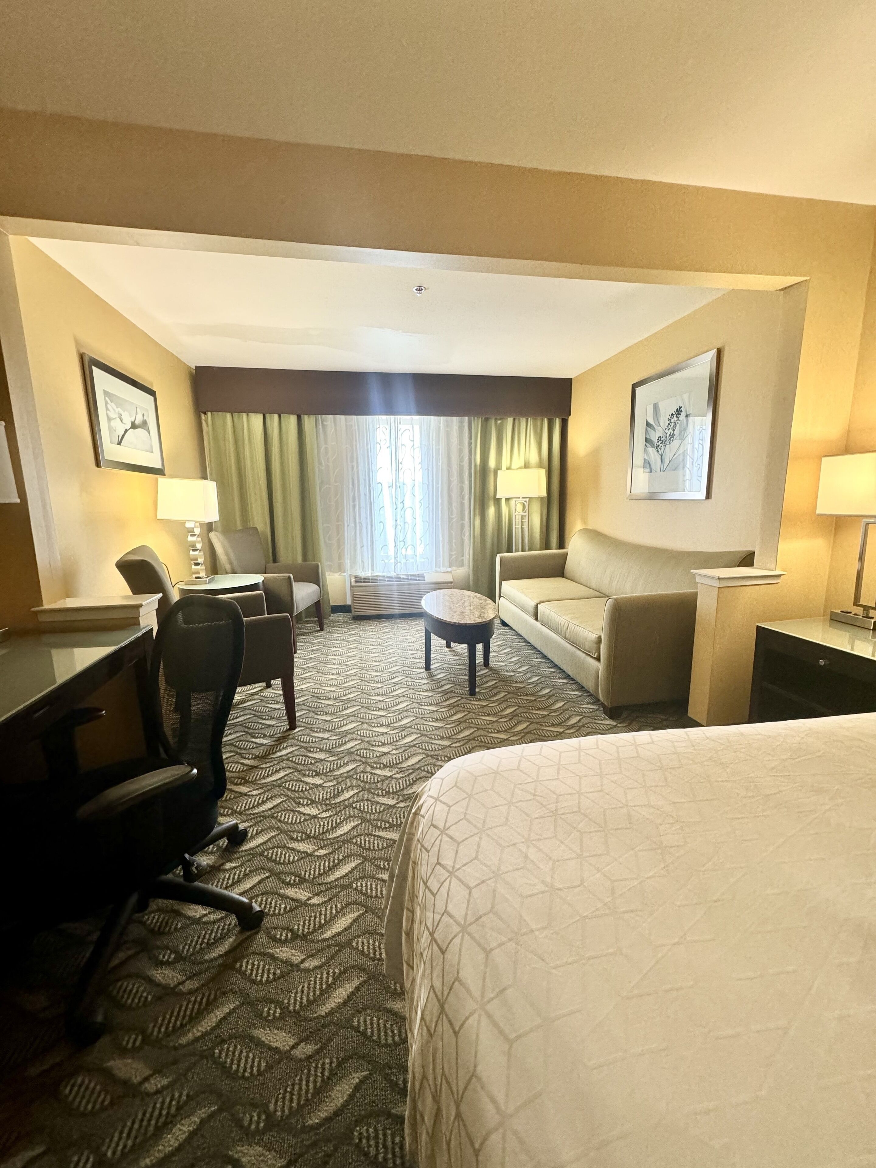 A hotel room with a large bed, a desk with a chair, a sofa, a coffee table, and a TV.
