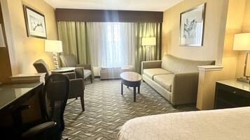 A hotel room with a large bed, a desk with a chair, a sofa, a coffee table, and a TV.