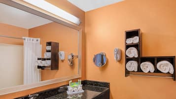 Un baño con un espejo grande, un perchero para toallas, un estante con toallas, un dispensador de jabón y un lavabo.