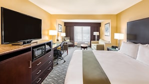 A hotel room with a large bed, a flat-screen TV, a desk with a chair, a small table, and two lamps.