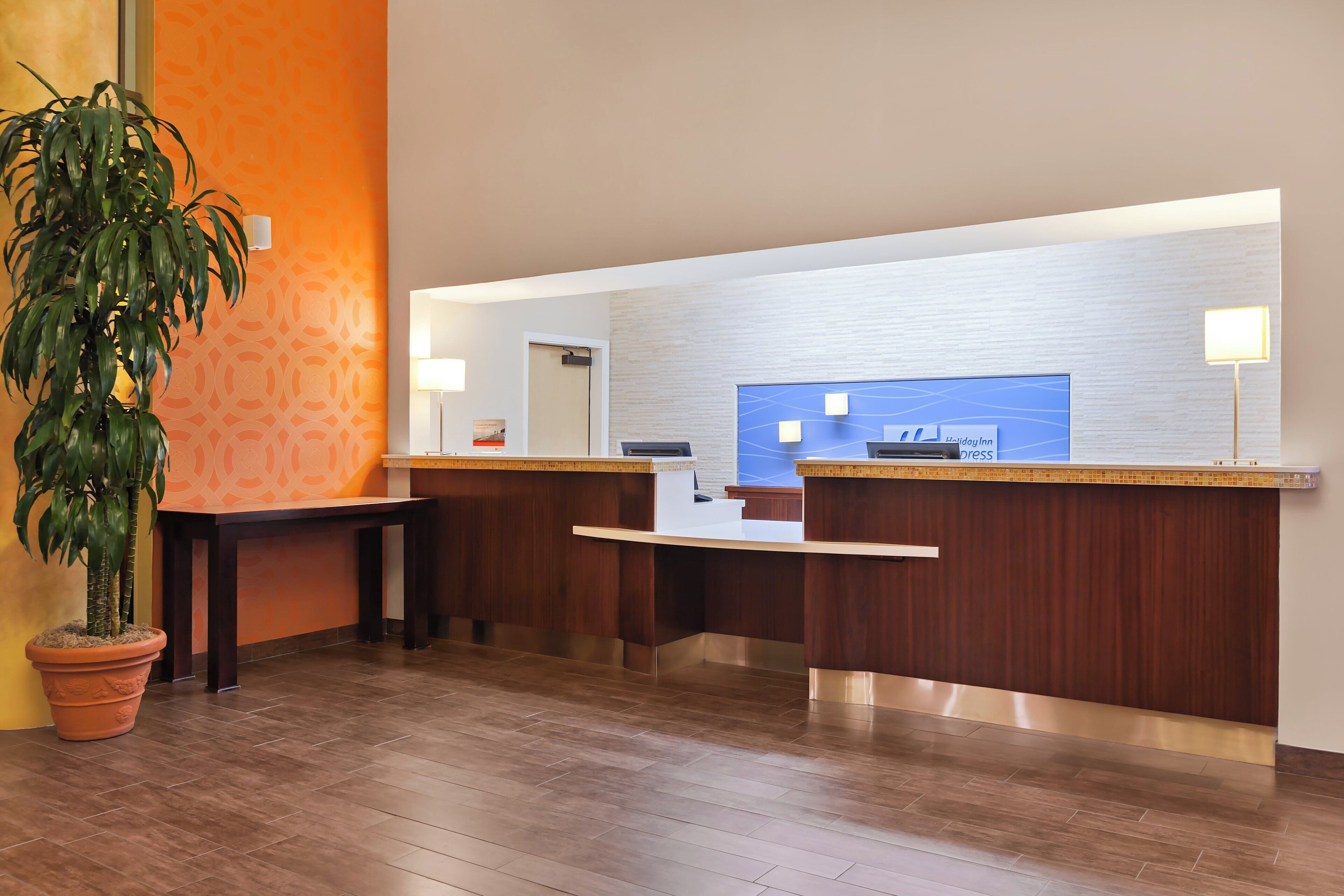 A reception area with a wooden reception desk, a potted plant, and a blue wall with a logo.
