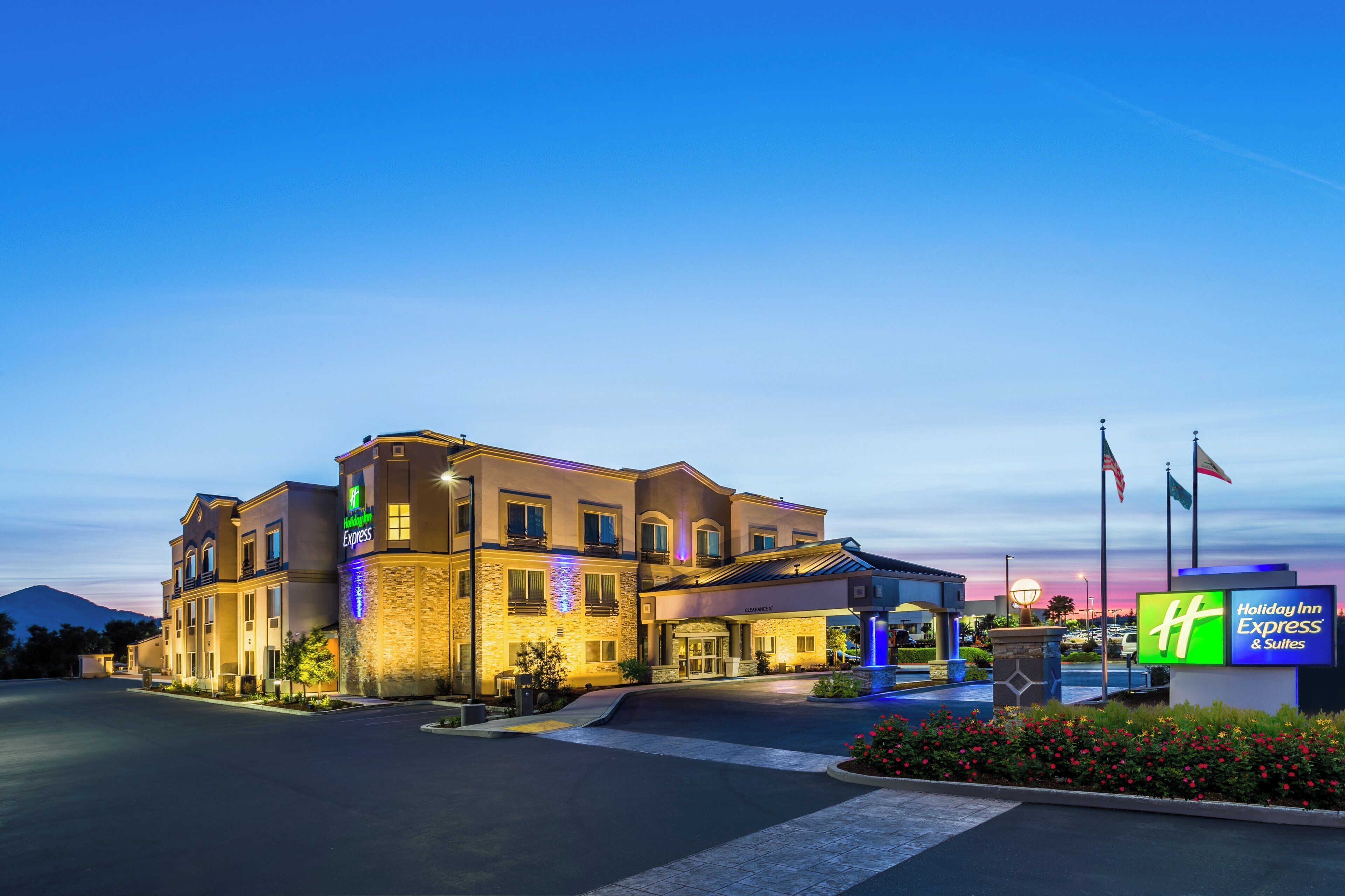 Un hotel Holiday Inn Express con una entrada despejada, un estacionamiento y una zona ajardinada con flores.