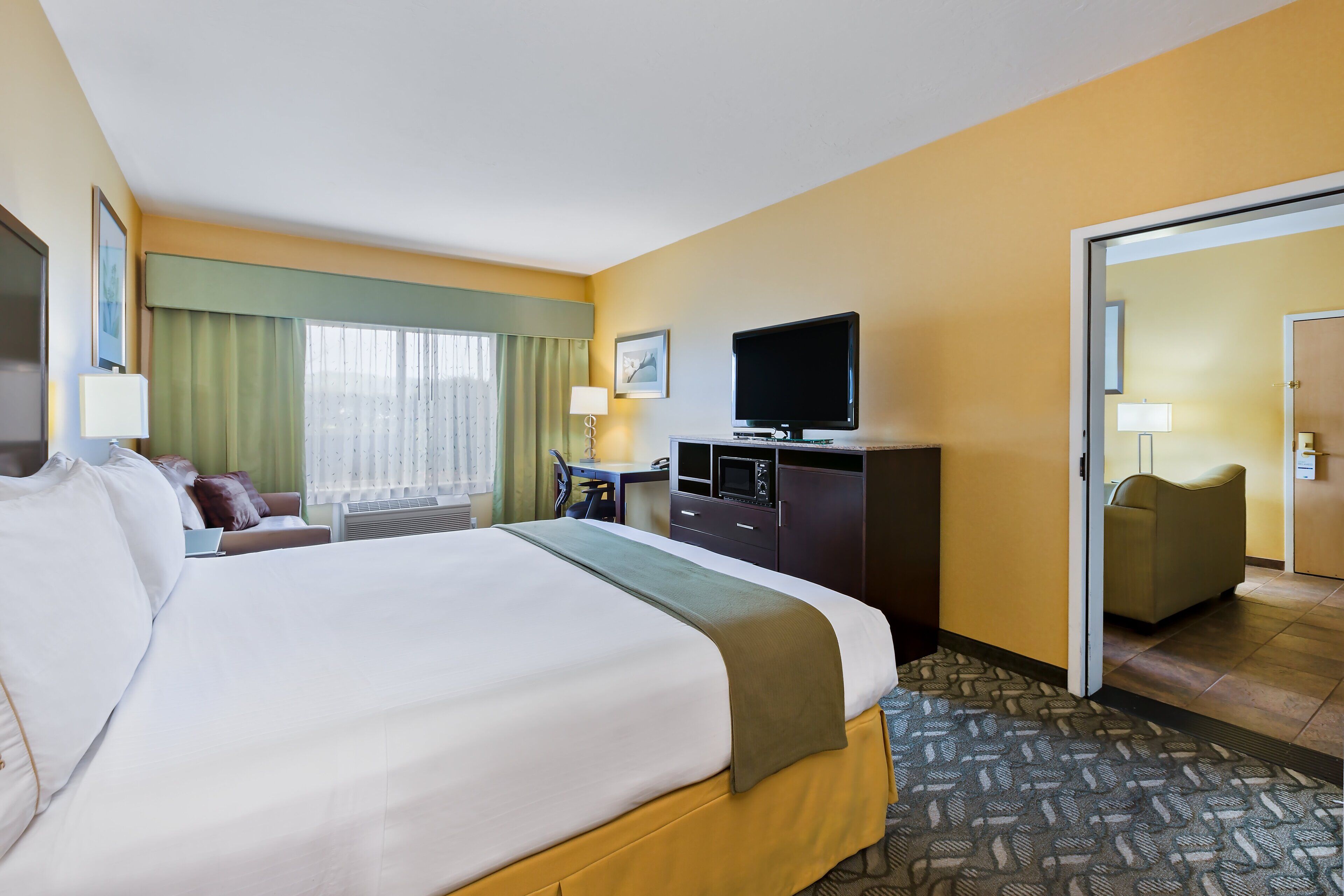 Une chambre d’hôtel avec un grand lit, un bureau avec un ordinateur, une télévision et une porte donnant sur une autre pièce.