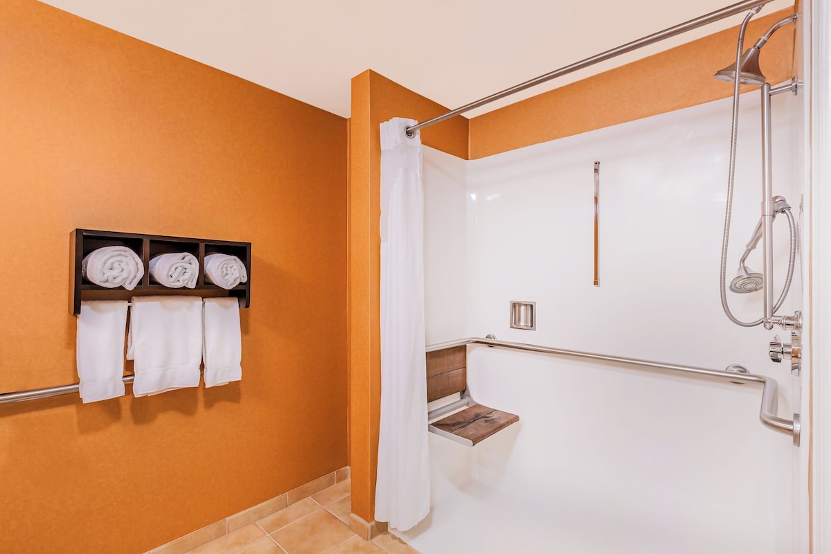 Un baño con ducha, un perchero con toallas y un estante de madera.