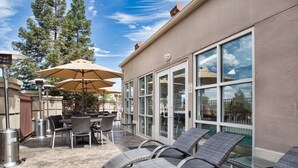 An outdoor patio with wicker lounge chairs, a table with chairs, and a large umbrella.