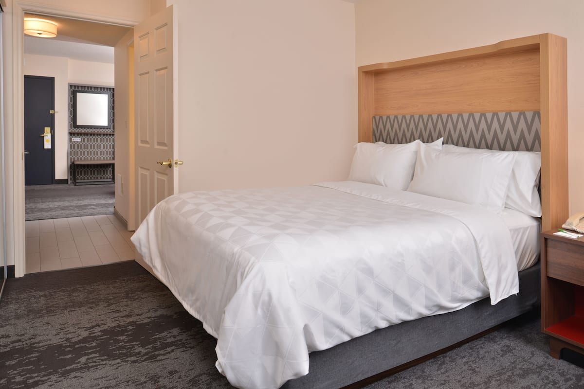 A hotel room with a large bed, a wooden headboard, a bedside table, and a carpeted floor.