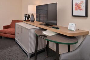 Ein Hotelzimmer mit Schreibtisch, Fernseher, Kaffeemaschine, Lampe und einem Schild mit dem Aufdruck 'Bleiben Sie verbunden'.