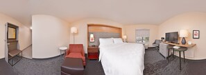 A hotel room with a bed, a desk, a chair, a small table, a TV, and a window with a view.