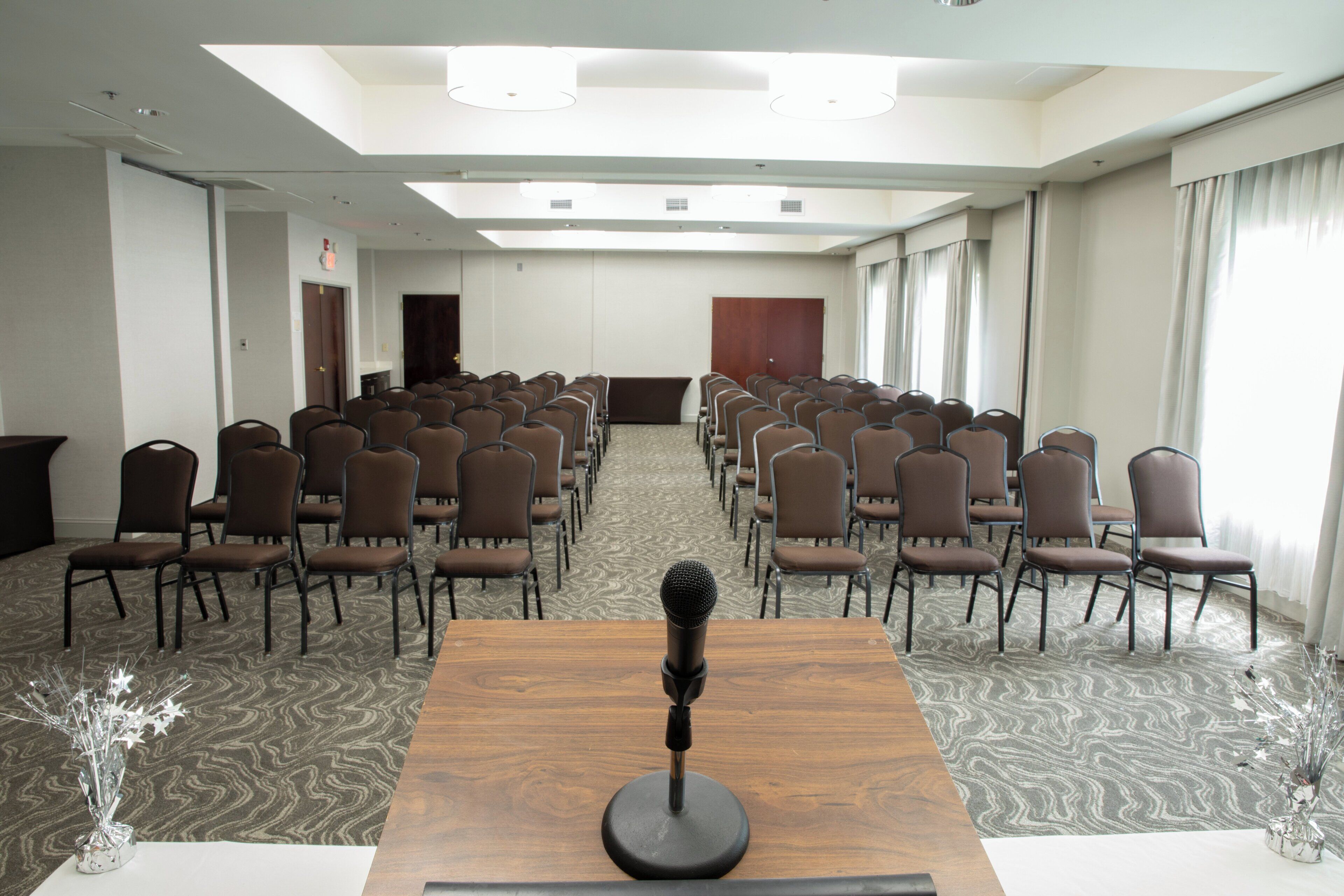Sala de conferências com fileiras de cadeiras, um púlpito e um tapete estampado.