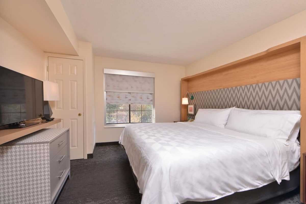 A hotel room with a bed, a TV, a dresser, and a window with blinds.