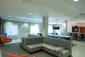 A modern hotel lobby with a sectional sofa, a bar area, and a dining space. - Holiday Inn Hotel & Suites Raleigh / Cary by IHG (Cary)