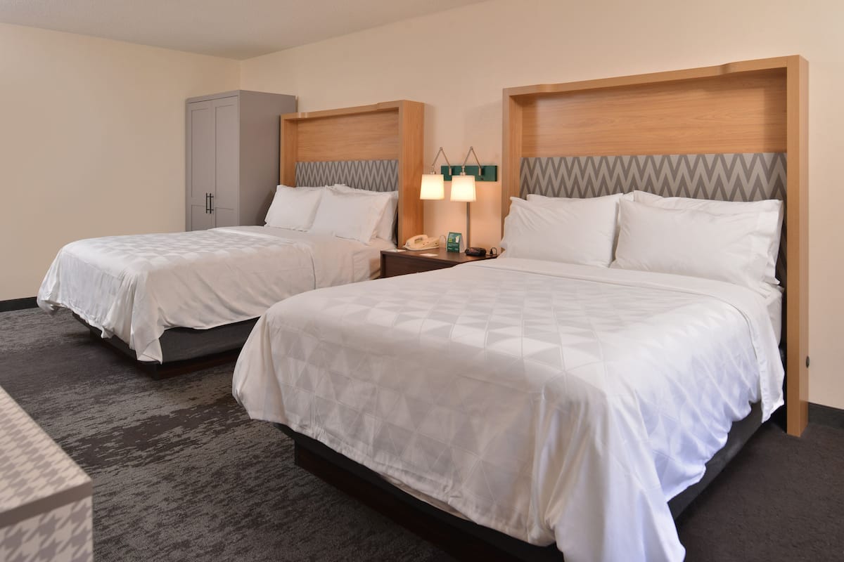 A hotel room with two beds, a wardrobe, a nightstand with a lamp, and a telephone.