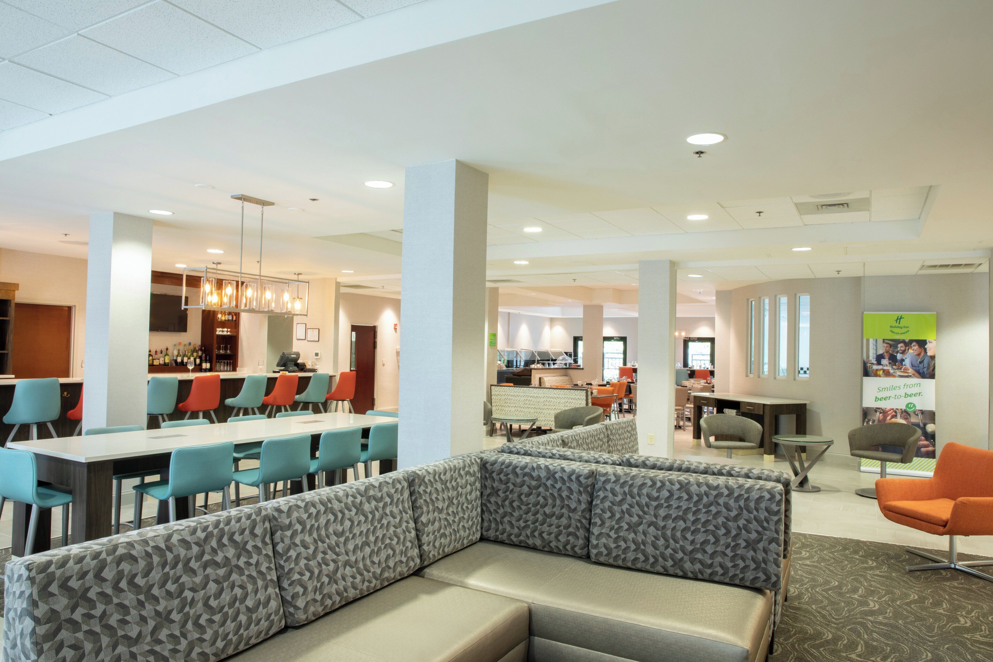 A modern hotel lobby with a bar area, seating arrangements, and a visible Holiday Inn sign.