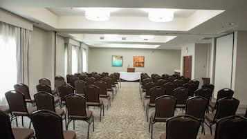 A conference room with rows of chairs facing a podium, a carpeted floor, and a large window with curtains.