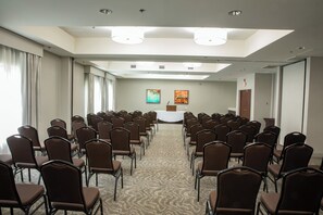 A conference room with rows of chairs facing a podium, a carpeted floor, and a large window with curtains. - Holiday Inn Hotel & Suites Raleigh / Cary by IHG (Cary)
