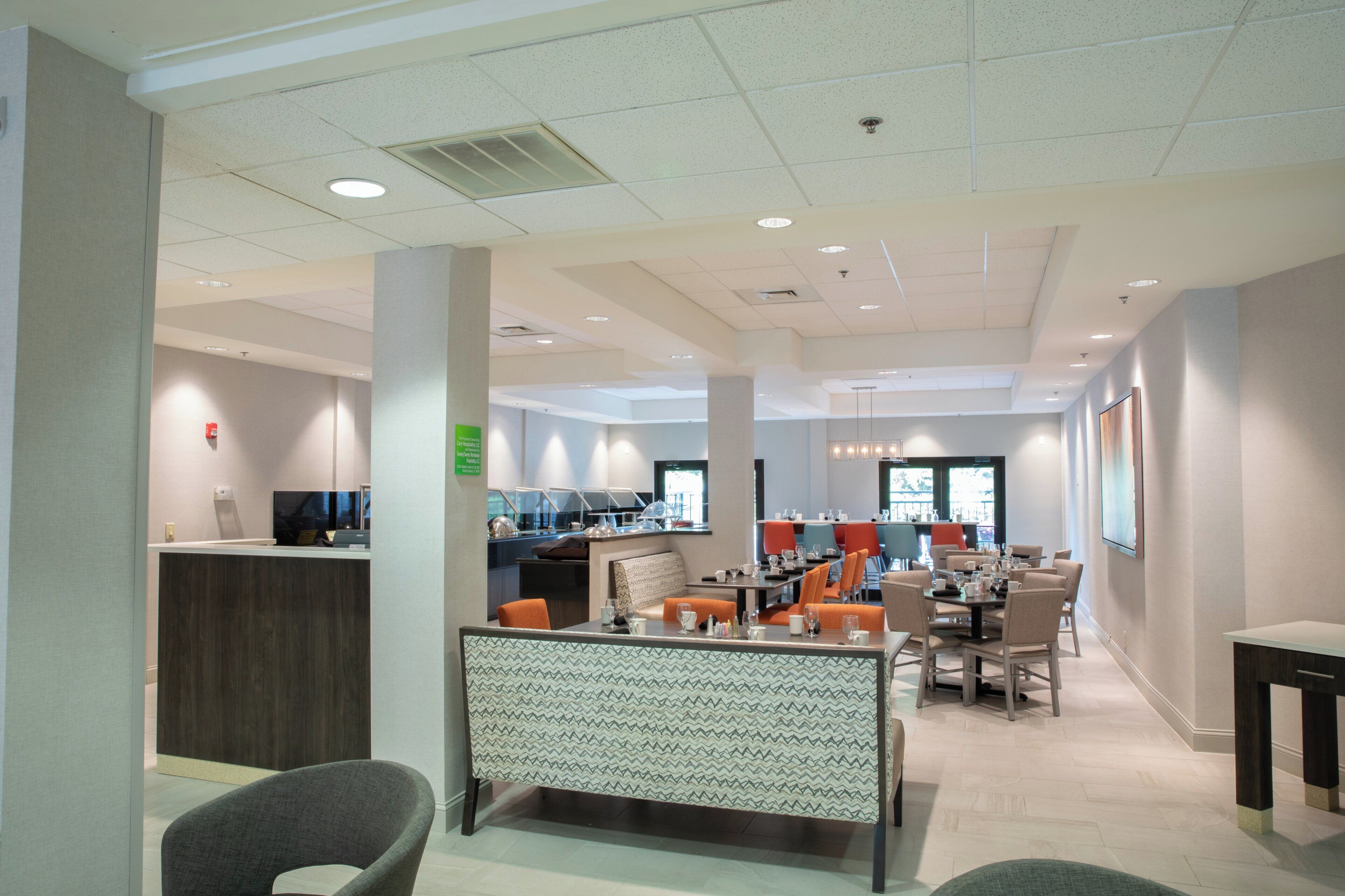 Een moderne hotellobby met een receptiebalie, zitgedeeltes en een eetruimte.