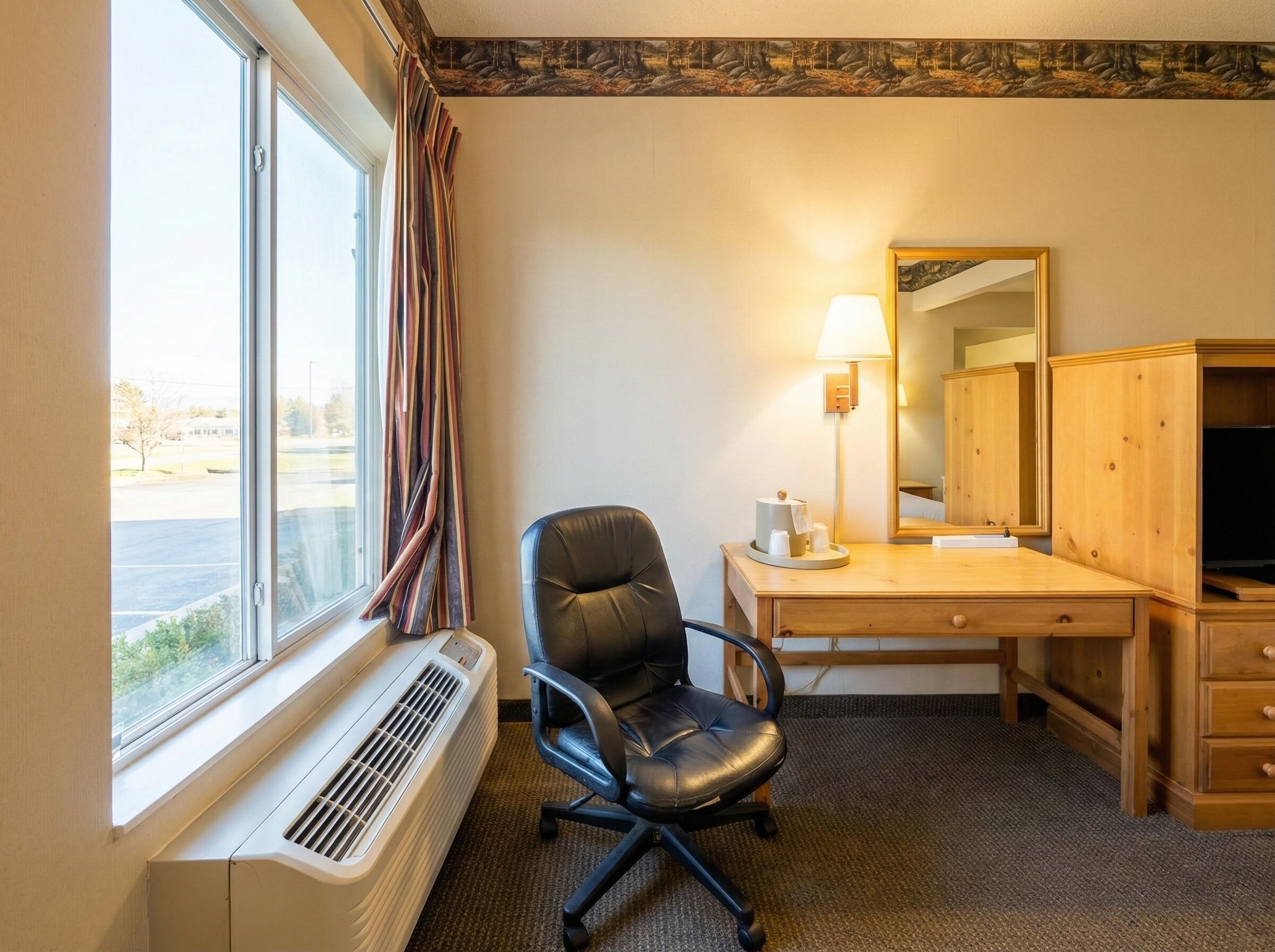 Habitación de hotel con un ventanal grande, un escritorio con silla, un espejo, un calefactor y un televisor.