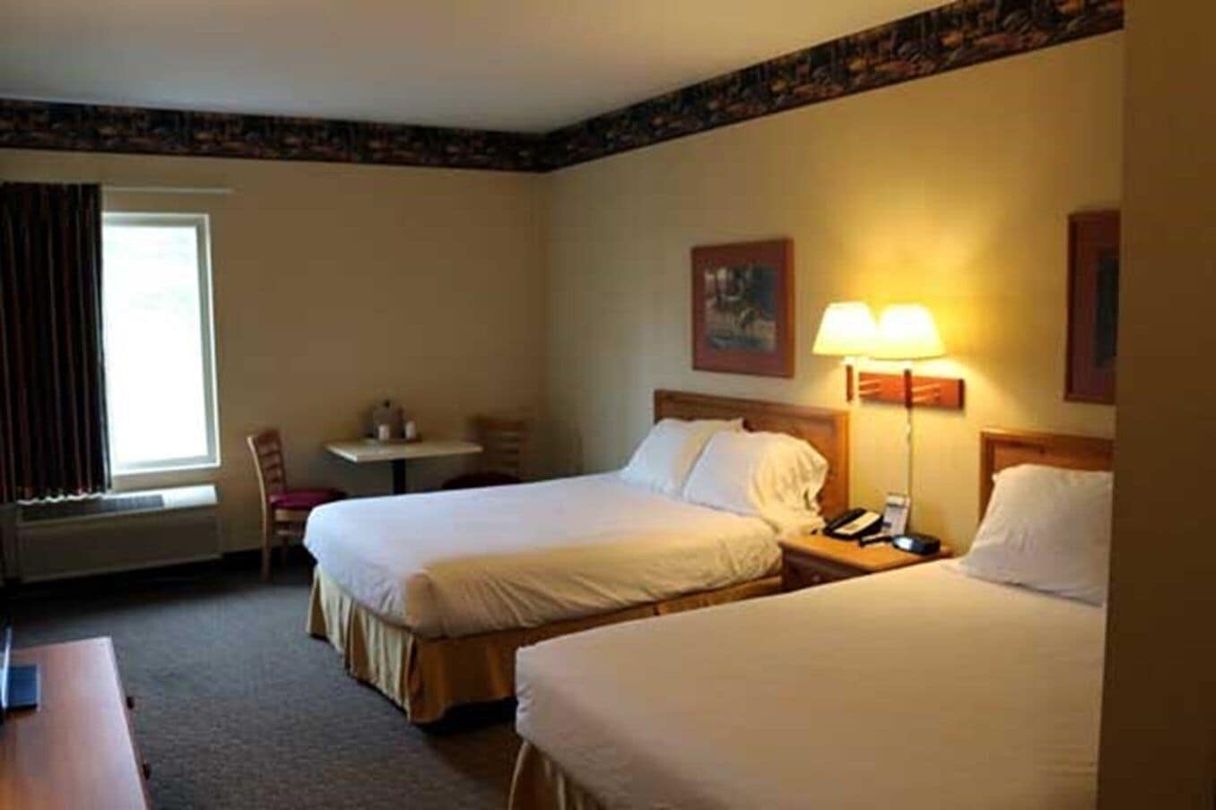 A hotel room with two beds, a desk, a chair, and a window with curtains.