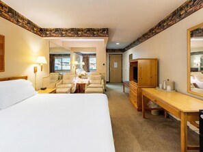 Una habitación de hotel con una cama grande, dos sillones, un escritorio de madera, una televisión y un espejo.