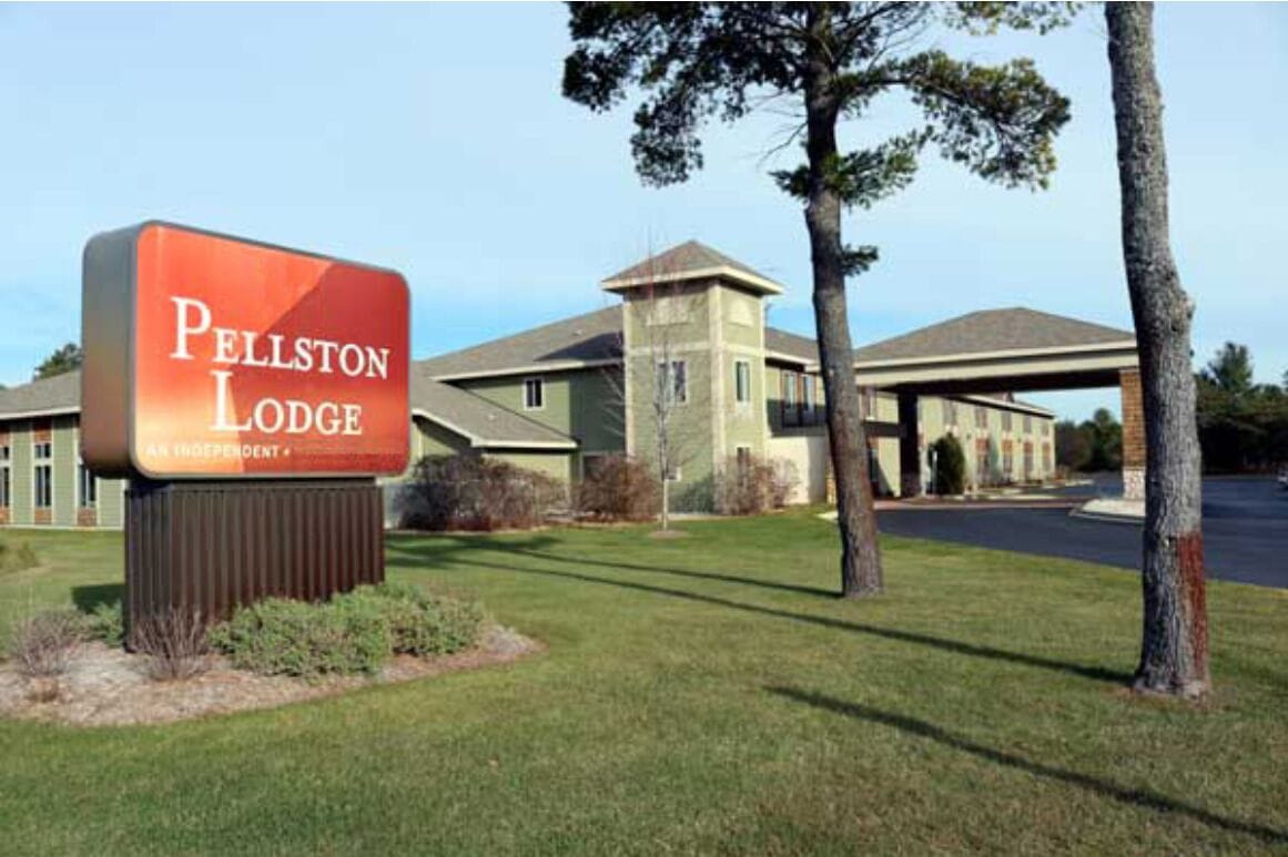 A sign for Pellston Lodge, an independent hotel with a modern building and a covered parking area.