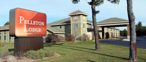 A sign for Pellston Lodge, an independent hotel with a modern building and a covered parking area.