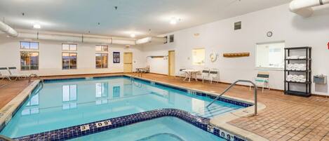 A large indoor swimming pool with clear lane markings, a tiled deck area, and a seating area with tables and chairs.