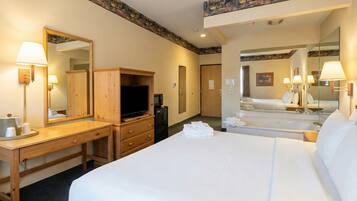 Habitación de hotel con una cama grande, un escritorio con televisor, un minibar y un baño con espejo.