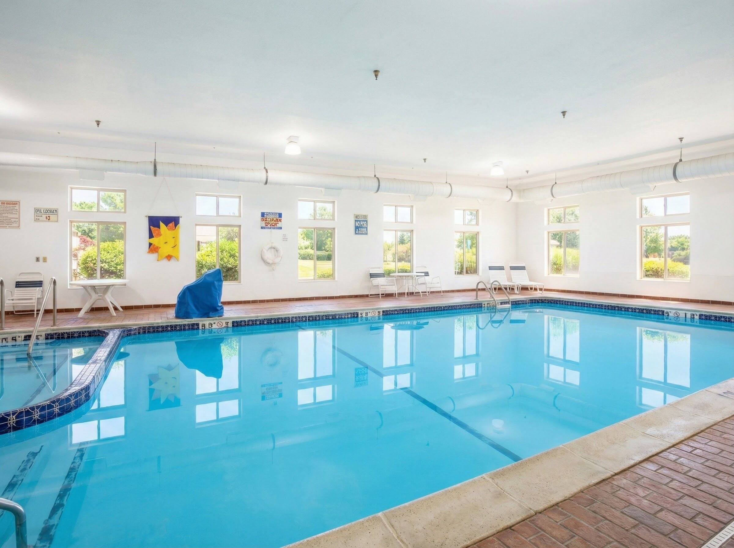 Una piscina interior con agua cristalina y azul, rodeada de ventanas y toldos.