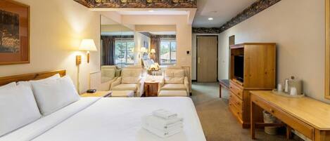 Una habitación de hotel con una cama grande, un escritorio, un televisor y una zona de estar con sillas.