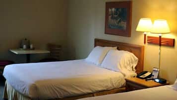 A hotel room with two beds, a bedside table with a lamp, a chair, and a painting on the wall.