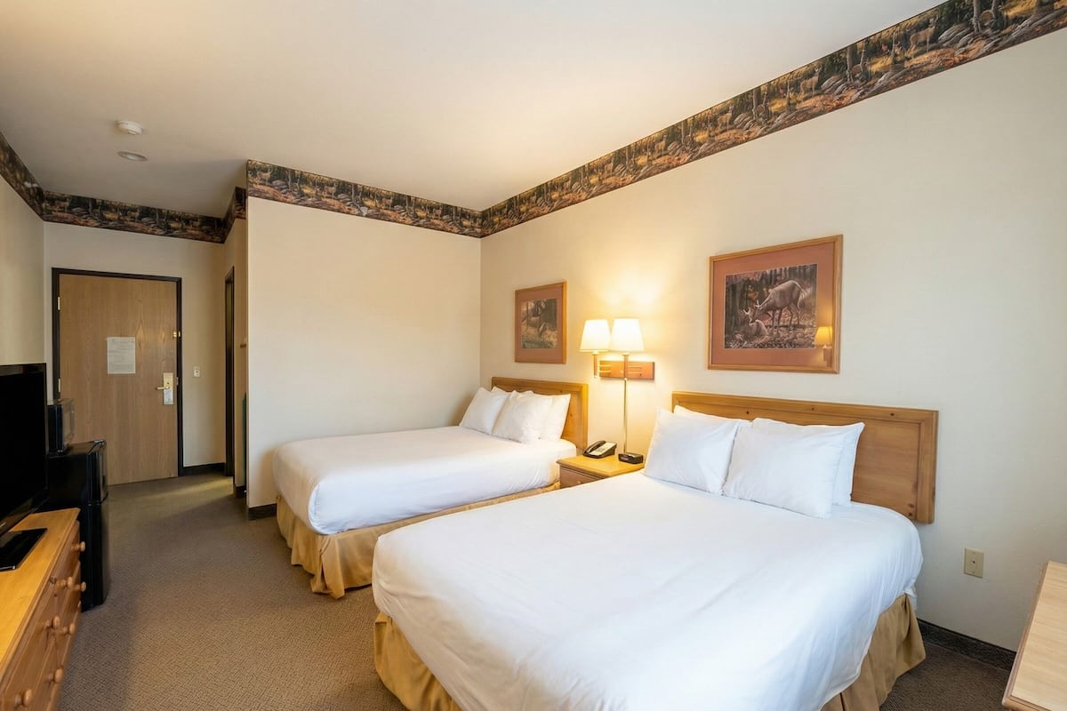 A hotel room with two beds, a desk, a TV, and a door.