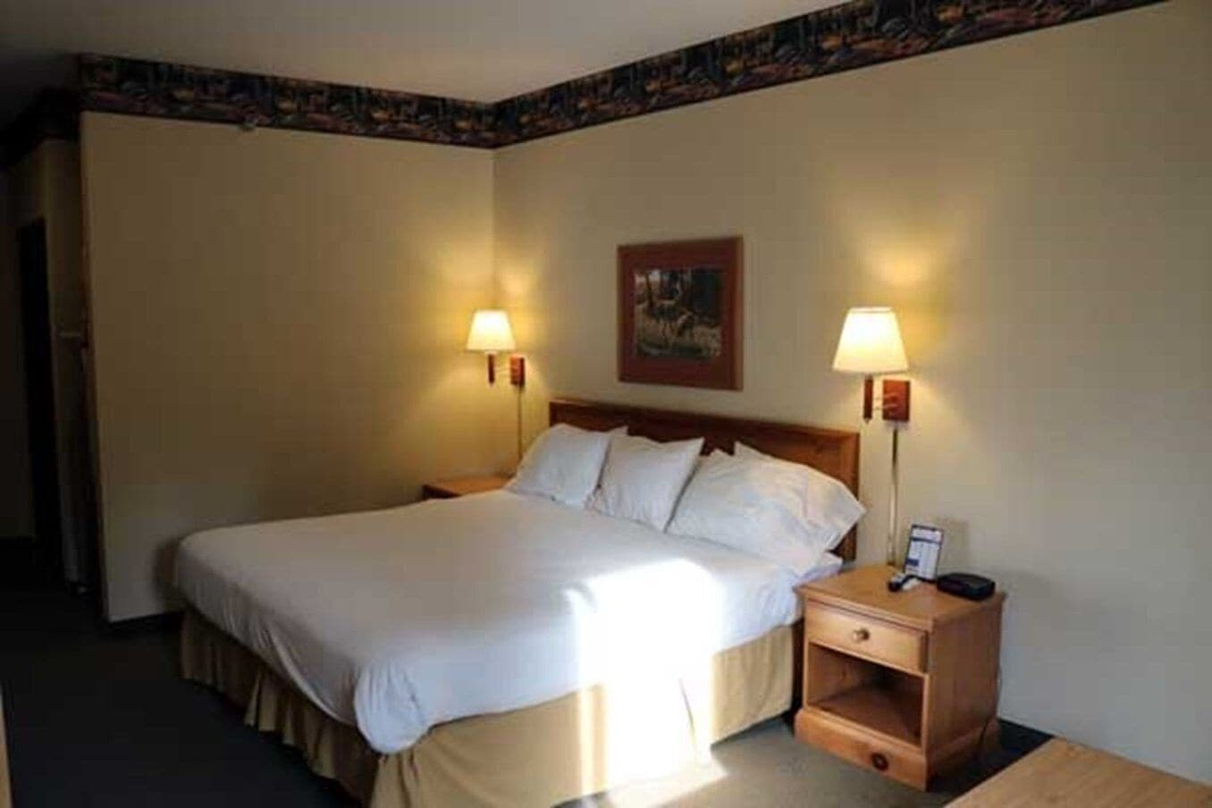 A hotel room with a large bed, two bedside lamps, a nightstand with a phone, and a painting on the wall.