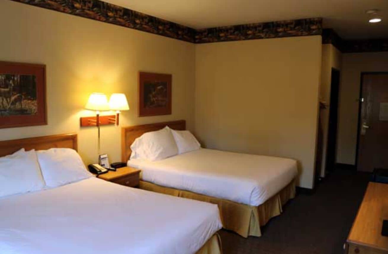 Een hotelkamer met twee enkele bedden, een nachtkastje met een lamp en een houten bureau.