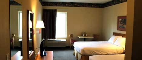 A hotel room with two beds, a desk, a chair, a lamp, and a window.