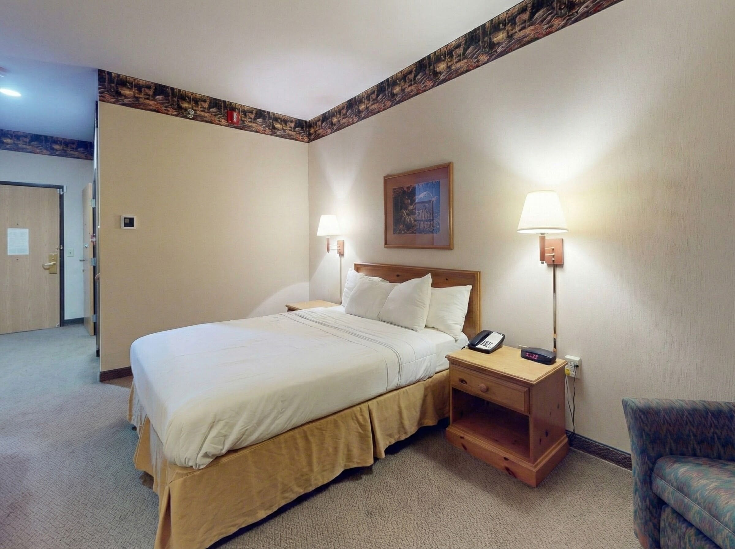 A hotel room with a large bed, two bedside lamps, a nightstand with a phone, and a framed picture on the wall.
