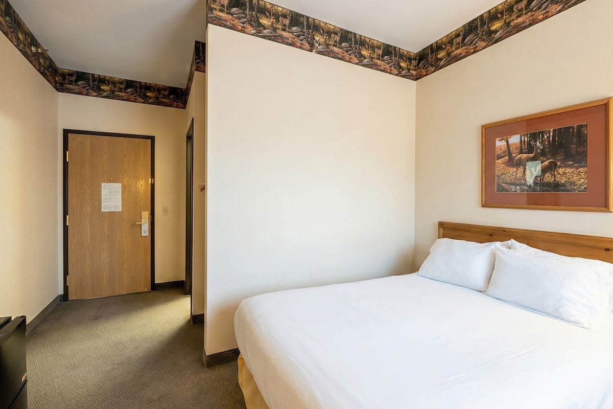 A hotel room with a large bed, a door, and a framed picture on the wall.