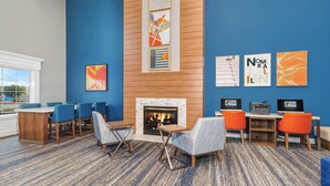 A hotel lobby with a fireplace, blue walls, and modern furniture. - Holiday Inn Express & Suites Bloomington - Normal by IHG (Normal)