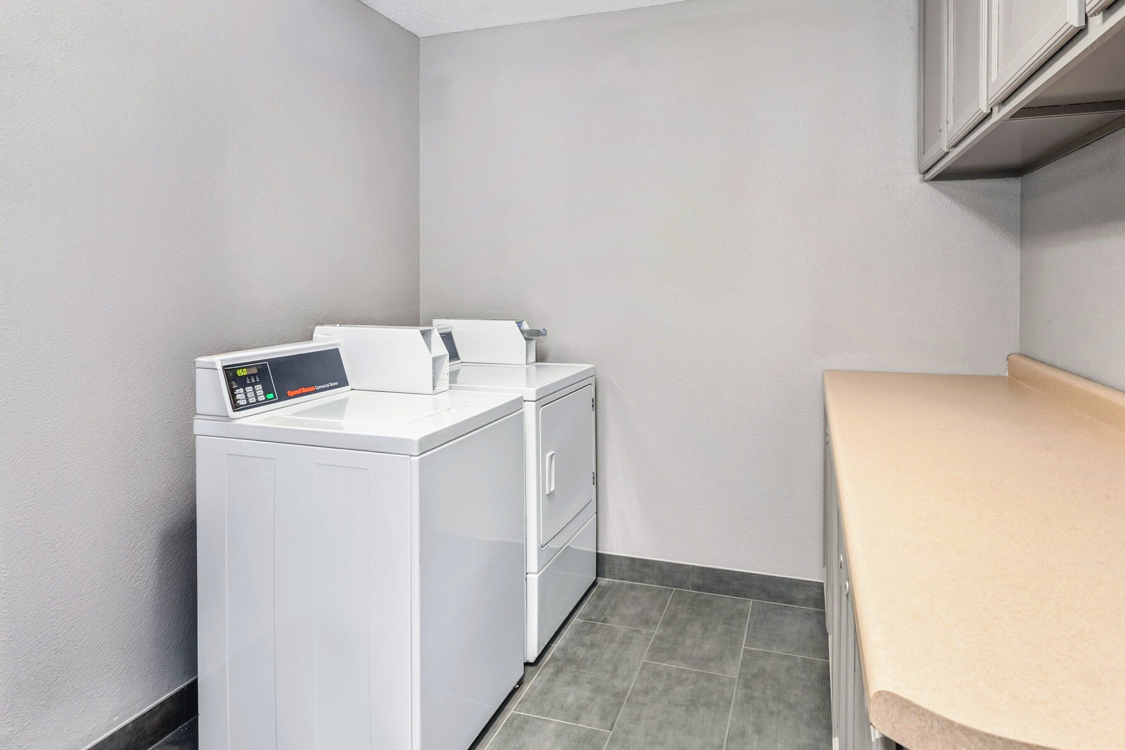 Un cuarto de lavandería con lavadora y secadora de carga frontal, una encimera y piso de baldosas.