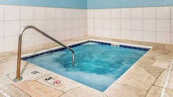 Ein kleines, quadratisches Whirlpool-Becken mit einer Metallleiter, gefliesten Wänden und einem gefliesten Boden.